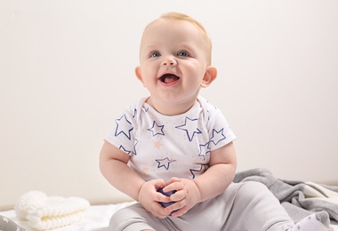 Little boy in cute clothes sitting on floor against light background. Baby accessories