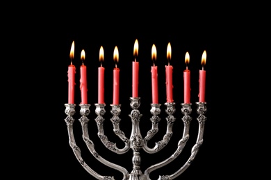 Photo of Silver menorah with burning candles against black background. Hanukkah celebration