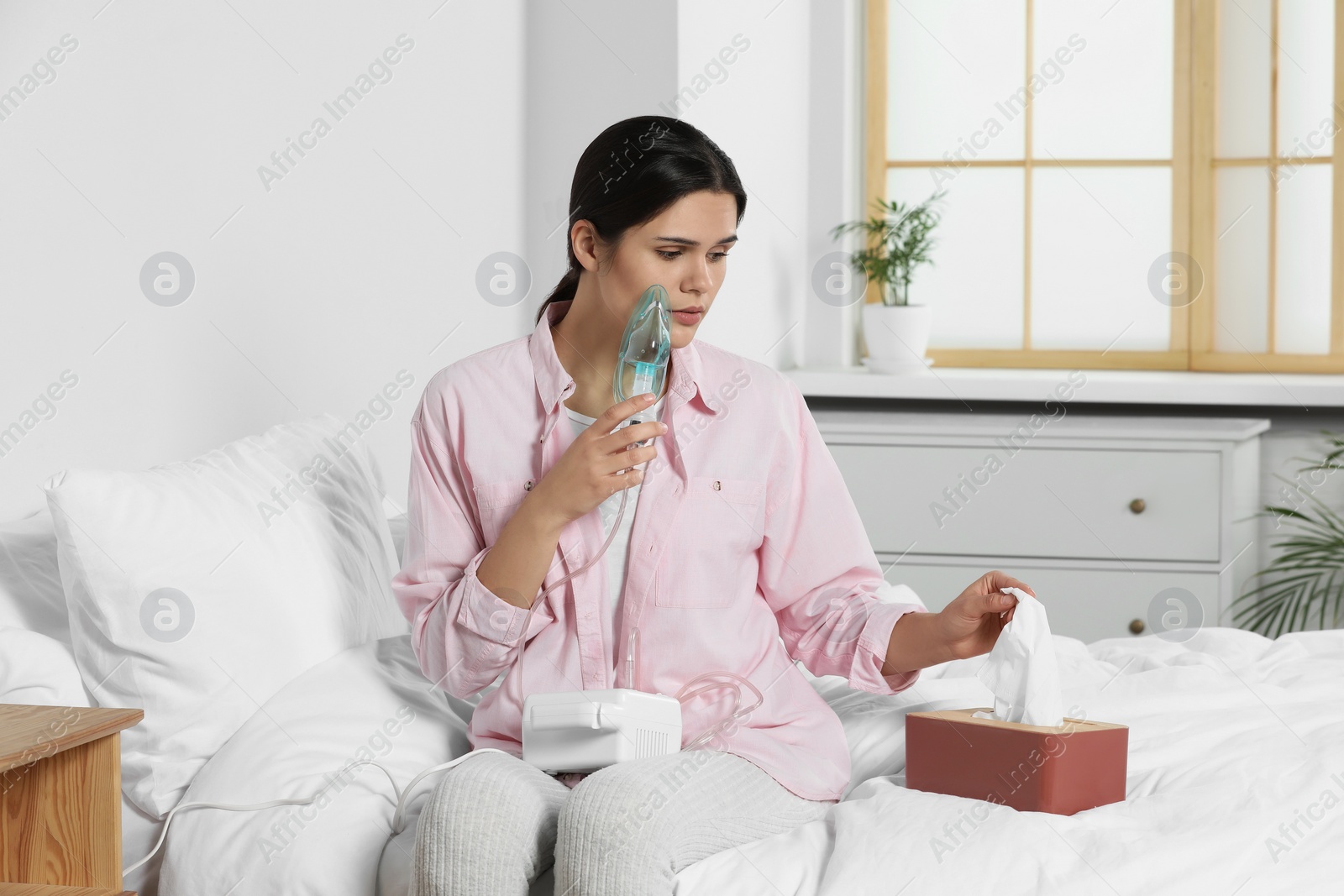 Photo of Sick young woman using nebulizer on bed at home