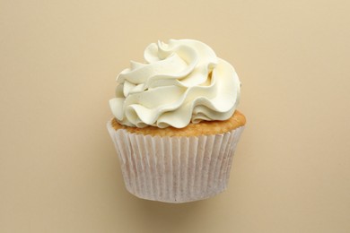 Tasty vanilla cupcake with cream on beige background, top view