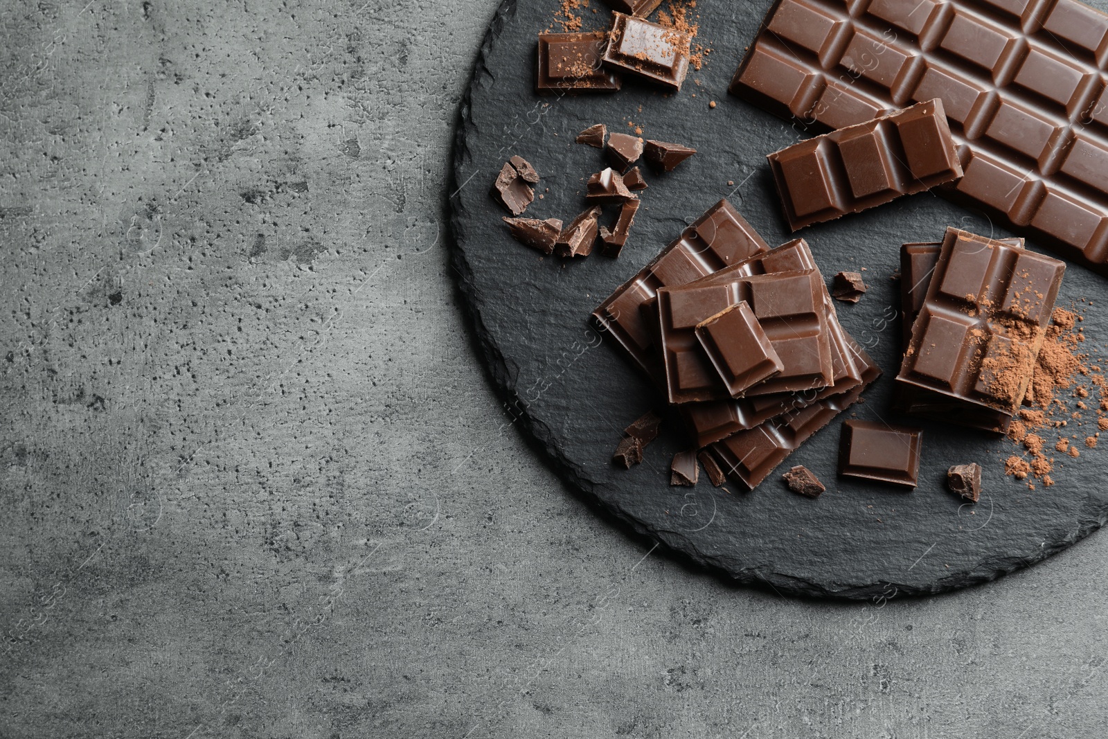 Photo of Slate plate with pieces of tasty chocolate on grey background, top view. Space for text