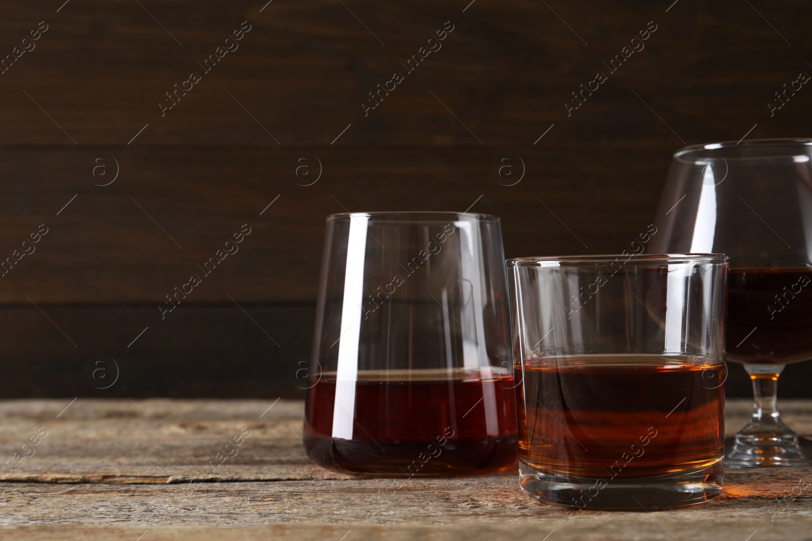 Photo of Different delicious liqueurs in glasses on wooden table, space for text