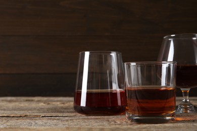 Different delicious liqueurs in glasses on wooden table, space for text
