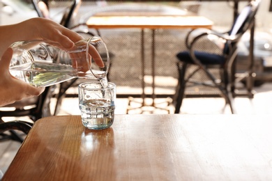 Photo of Woman pouring water into glass on wooden table indoors