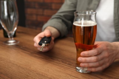 Photo of Man with glass of alcoholic drink holding car key at table, closeup. Don't drink and drive concept