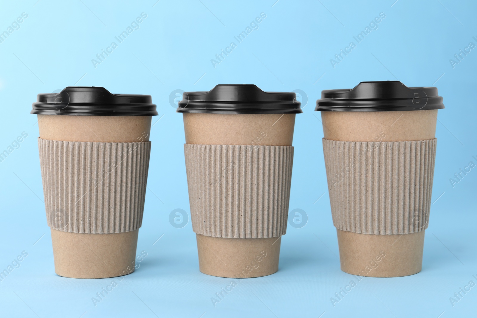 Photo of Paper cups with black lids on light blue background. Coffee to go