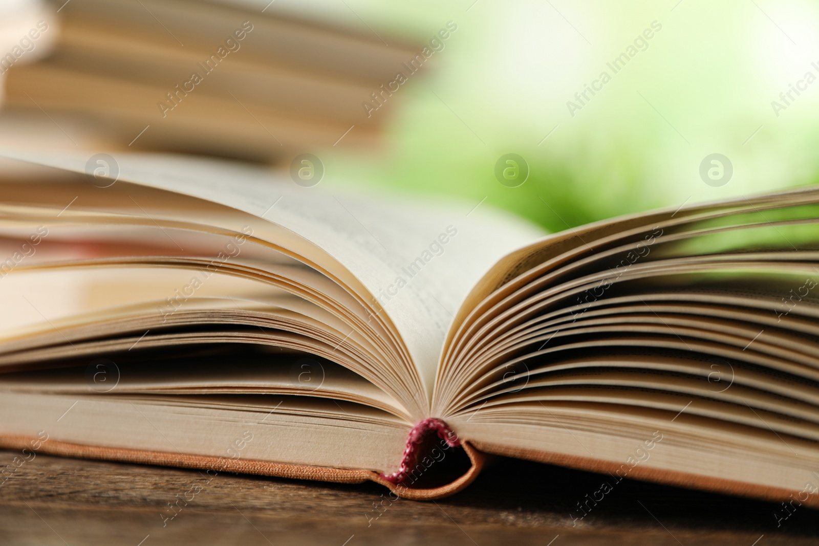 Photo of Open hardcover book on wooden table against blurred background, closeup