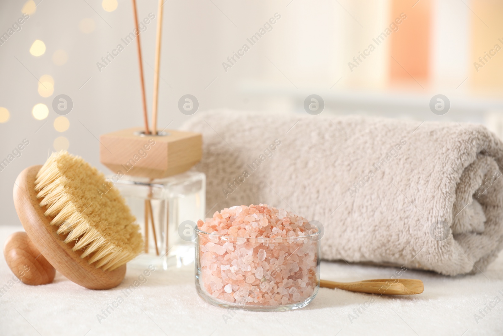 Photo of Spa composition. Sea salt, brush, towel and reed air freshener on soft white surface