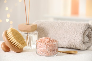 Photo of Spa composition. Sea salt, brush, towel and reed air freshener on soft white surface