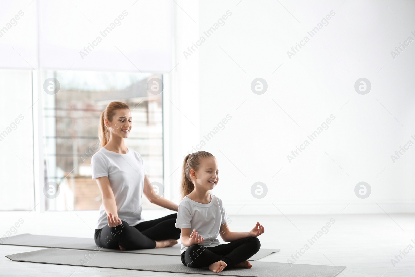 Photo of Mother and daughter in matching sportswear doing yoga together at home