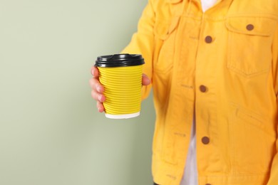 Photo of Woman holding takeaway cup with drink on pale green background, closeup view and space for text. Coffee to go
