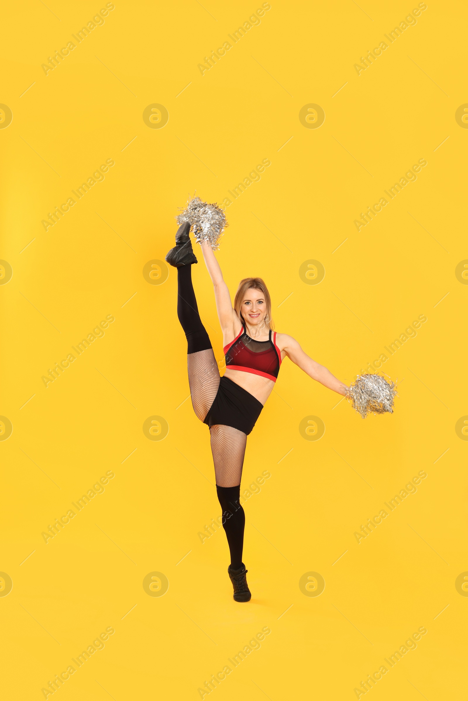 Photo of Beautiful cheerleader in costume holding pom poms on yellow background