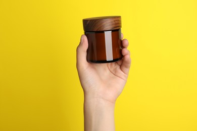 Photo of Woman holding jar of face cream on yellow background, closeup