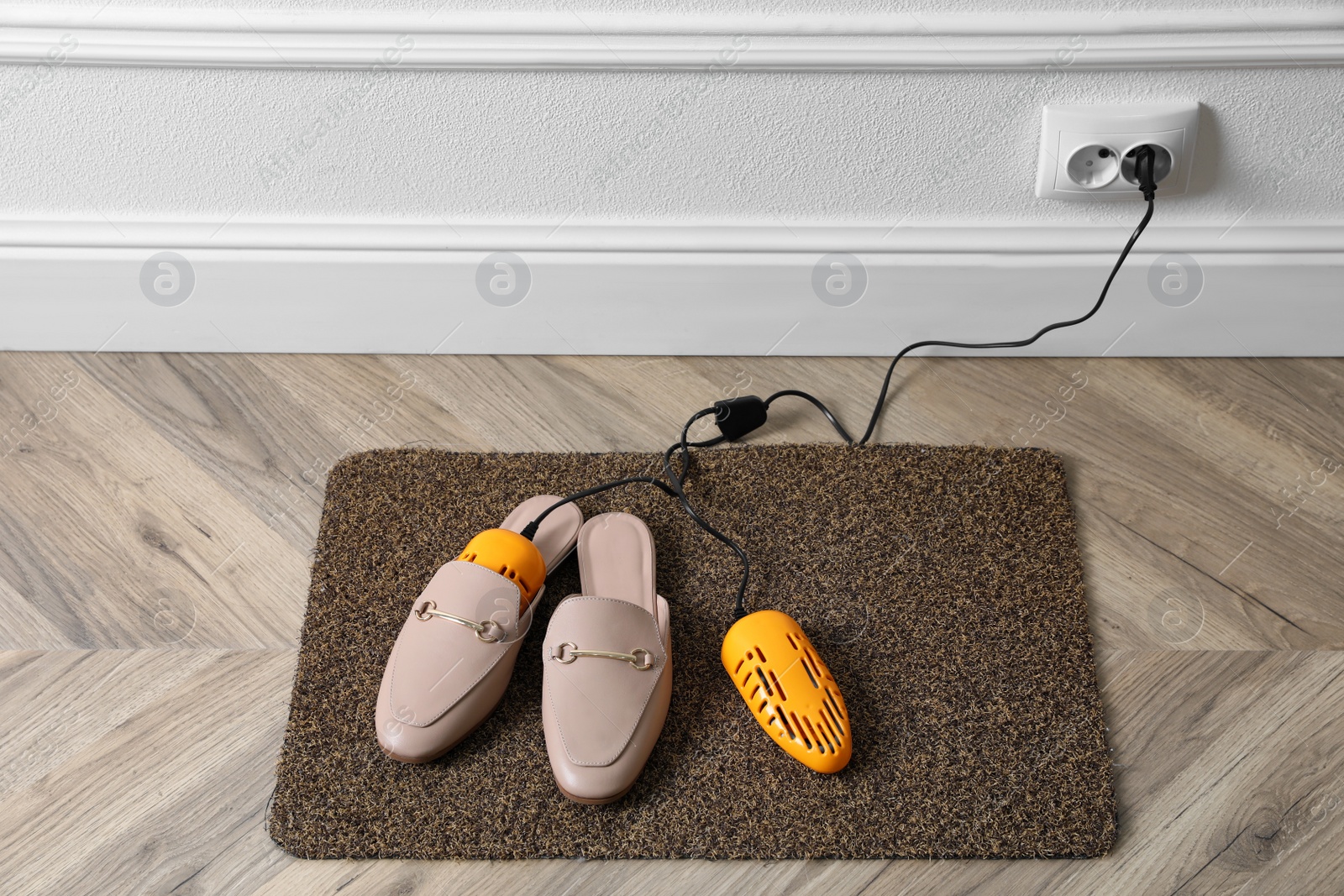 Photo of Pair of stylish shoes with modern electric footwear dryer on door mat indoors