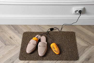 Pair of stylish shoes with modern electric footwear dryer on door mat indoors