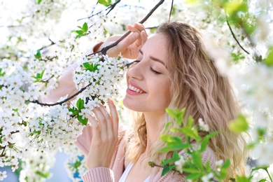 Photo of Attractive young woman posing near blossoming tree on sunny spring day