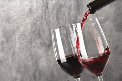 Pouring red wine into glass against grey background, closeup. Space for text