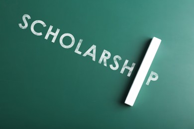 Word SCHOLARSHIP and piece of chalk on green chalkboard, top view