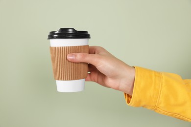 Woman holding takeaway cup with drink on pale green background, closeup. Coffee to go