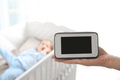 Photo of Woman holding baby monitor near crib with child in room. Video nanny