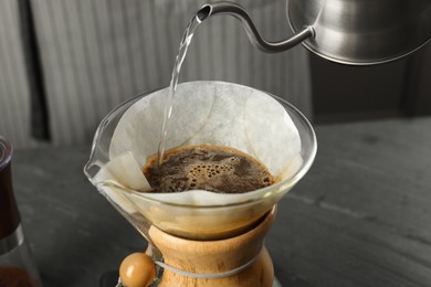 Photo of Pouring hot water into glass chemex coffeemaker with paper filter and coffee on gray table, closeup