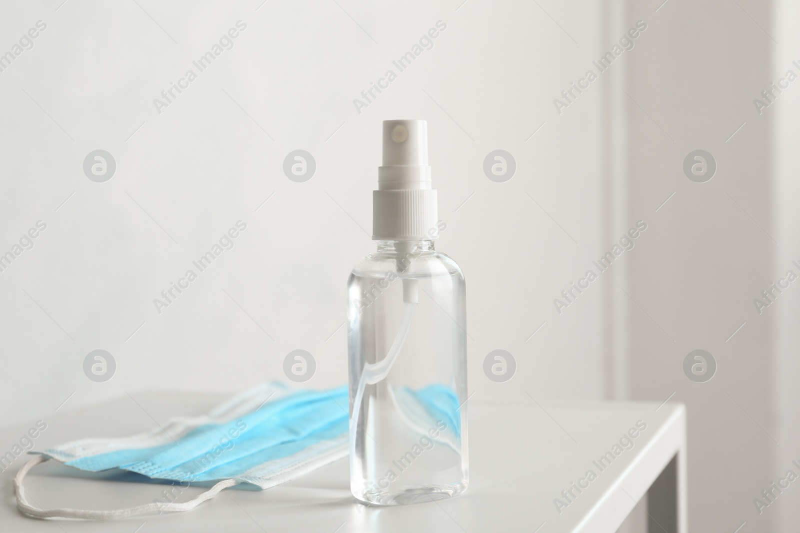 Photo of Antiseptic spray and protective mask on table indoors. Protection from virus