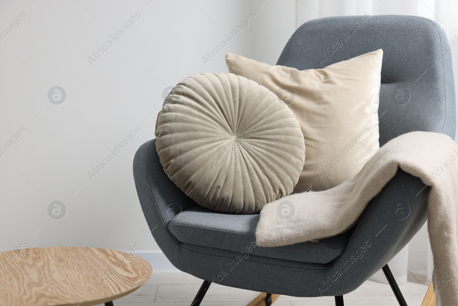 Photo of Soft pillows and blanket on rocking armchair near side table indoors