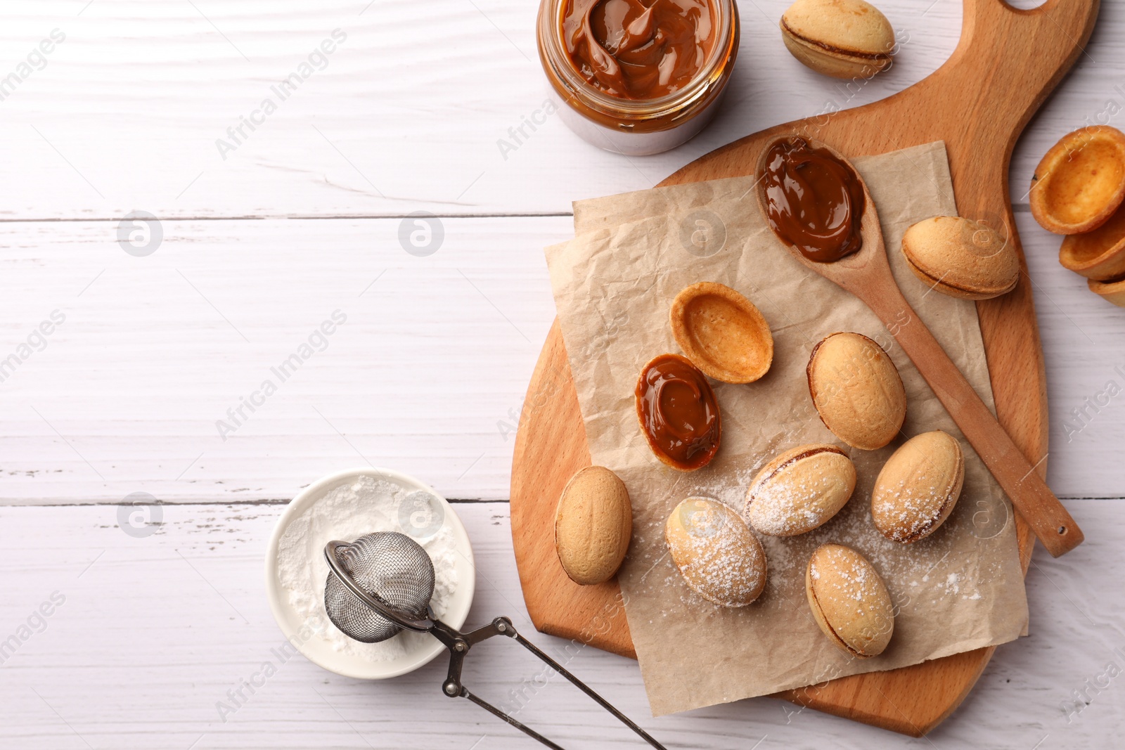 Photo of Delicious nut shaped cookies with boiled condensed milk and powdered sugar on white wooden table, flat lay