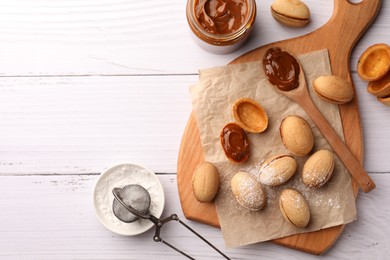 Delicious nut shaped cookies with boiled condensed milk and powdered sugar on white wooden table, flat lay