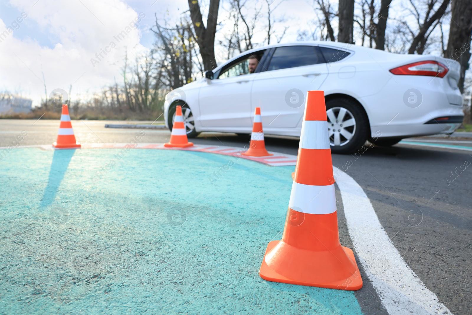 Photo of Young man in car at test track, focus on traffic cone. Driving school