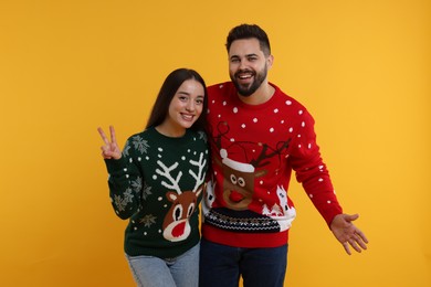 Photo of Happy young couple in Christmas sweaters on orange background