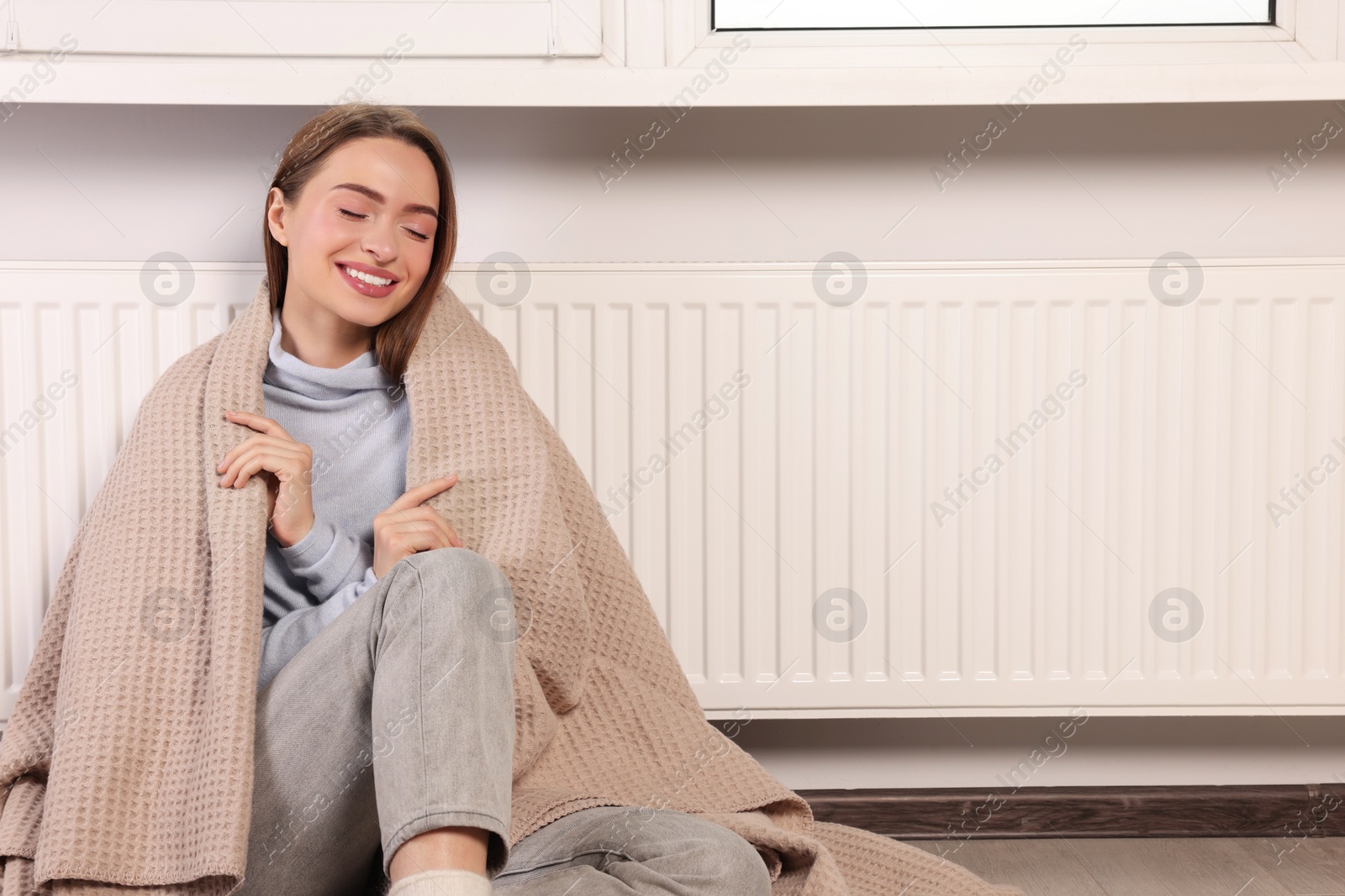 Photo of Woman with blanket near heating radiator indoors, space for text