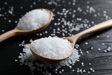 Organic salt in spoons on black wooden table, closeup