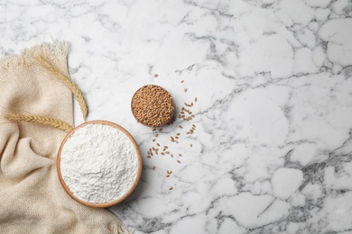 Bowl with wheat flour and grains on marble background