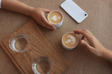Photo of Friends drinking coffee at wooden table in cafe, top view