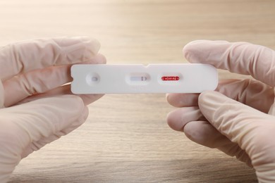 Photo of Doctor holding disposable Covid-19 express test at wooden table, closeup