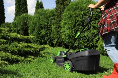 Woman cutting grass with lawn mower in garden on sunny day, closeup