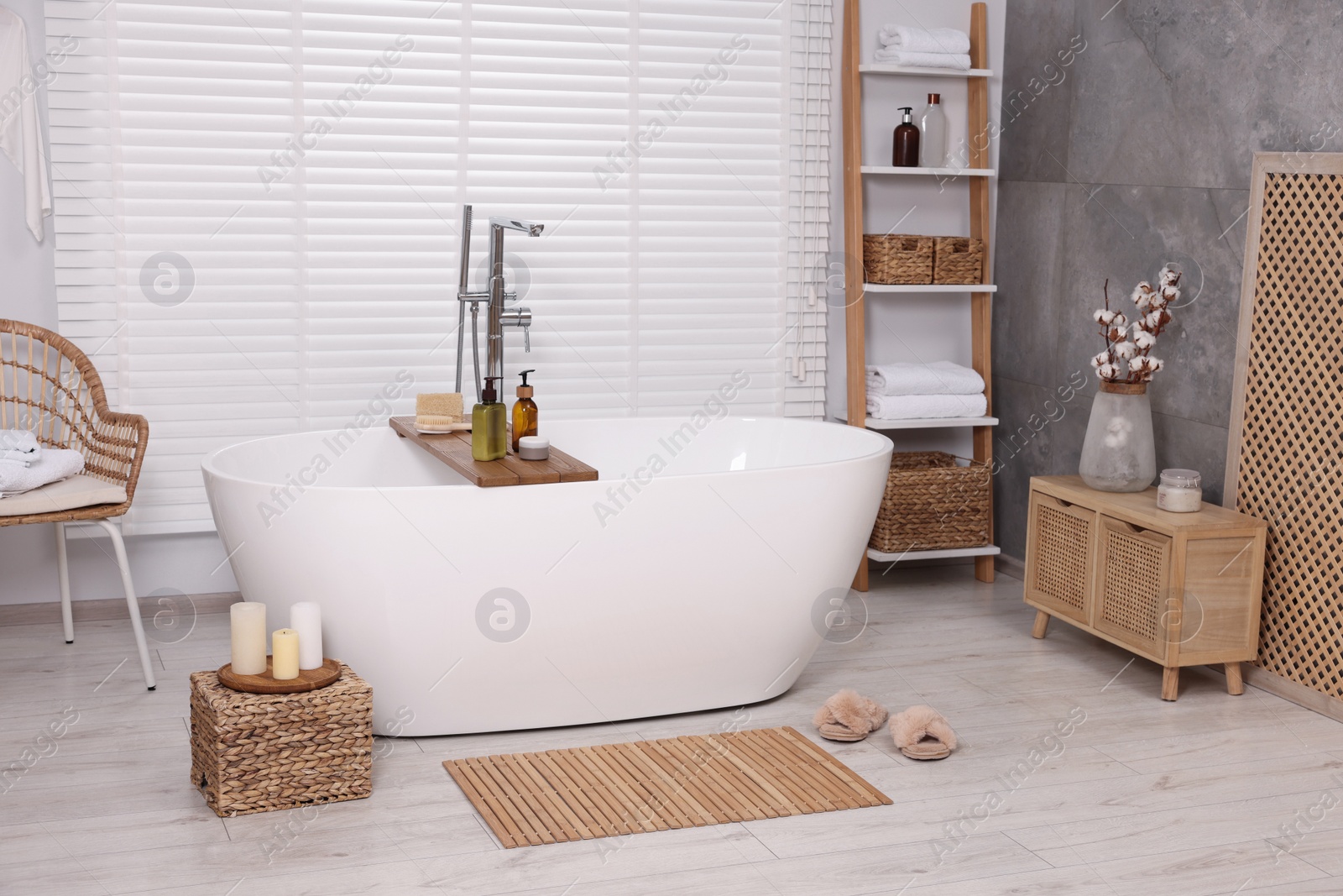 Photo of Stylish bathroom interior with bamboo bath mat and white tub