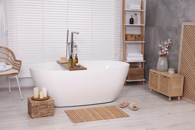 Photo of Stylish bathroom interior with bamboo bath mat and white tub