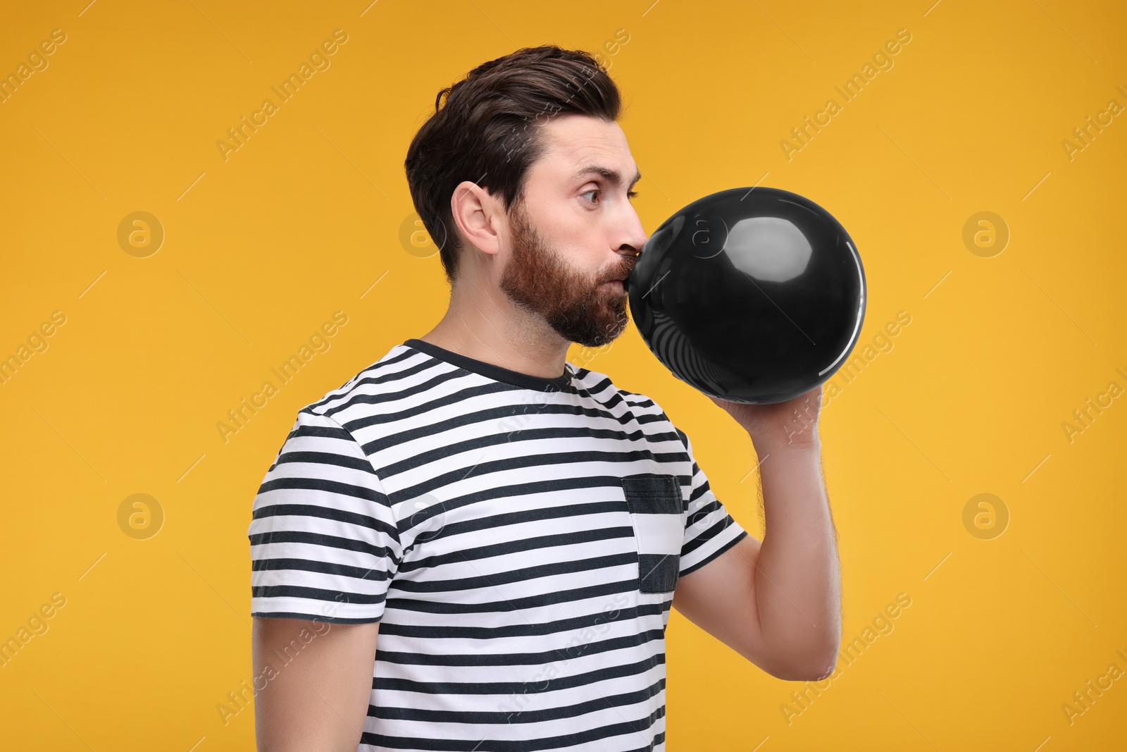 Photo of Man inflating black balloon on yellow background