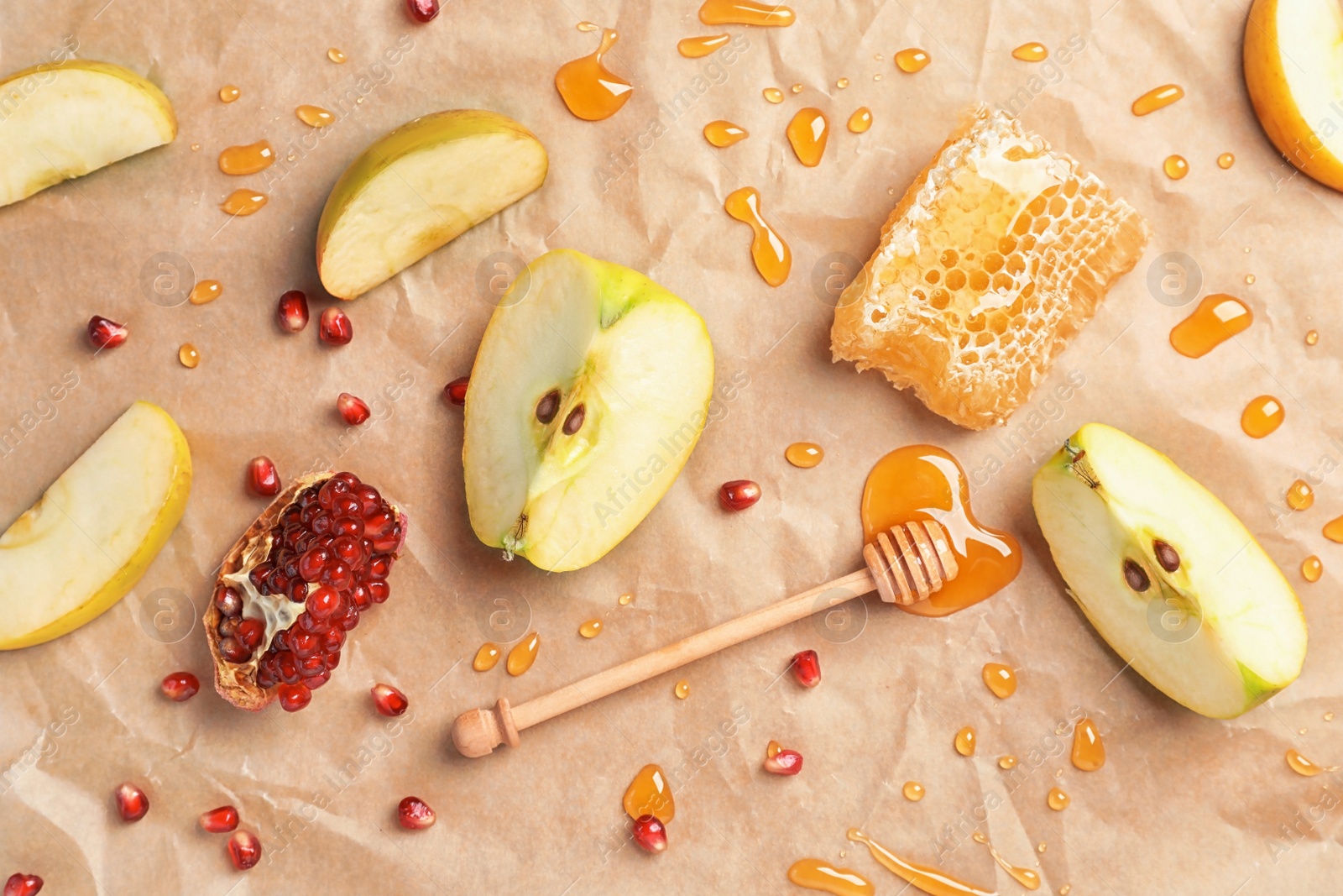 Photo of Flat lay composition with drops of honey, dipper, sliced apples and pomegranate on parchment paper. Rosh Hashanah holiday