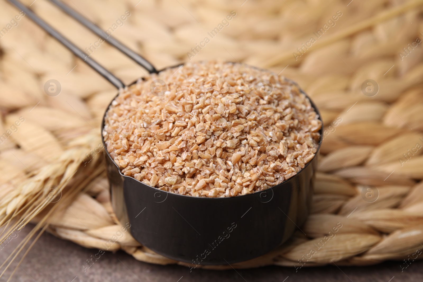 Photo of Dry wheat groats in scoop and spikelet on table, closeup