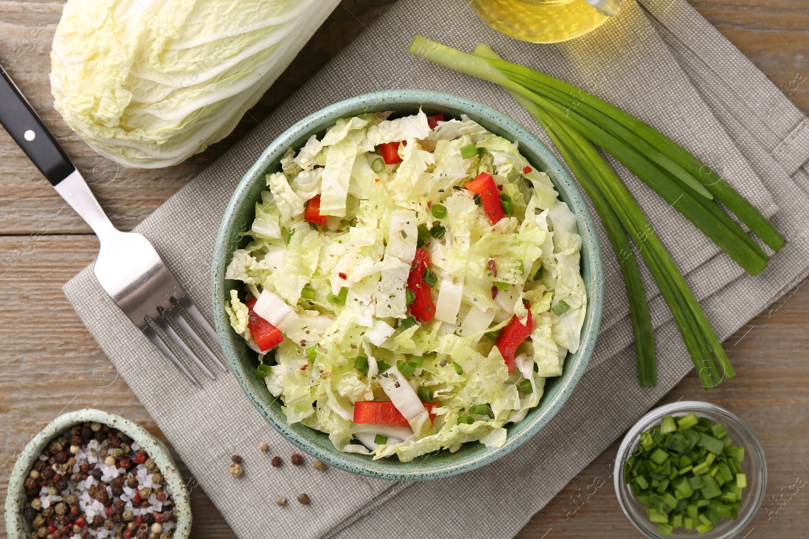 Photo of Tasty salad with Chinese cabbage in bowl, spices and ingredients on wooden table, flat lay