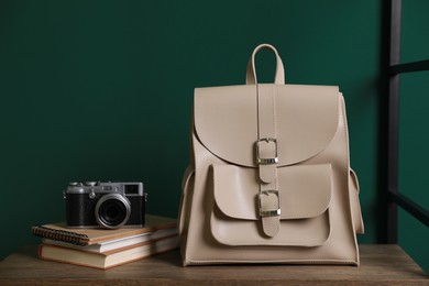 Stylish urban backpack, books and camera on shelf near green wall