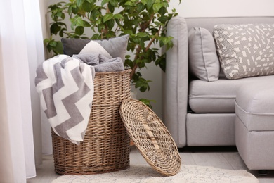 Photo of Basket with blankets and pillow near sofa indoors