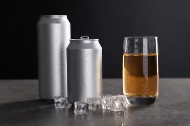 Energy drink in glass, aluminium cans and ice cubes on grey table