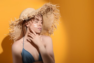 Photo of Beautiful young woman in straw hat with sun protection cream on her face against orange background, space for text