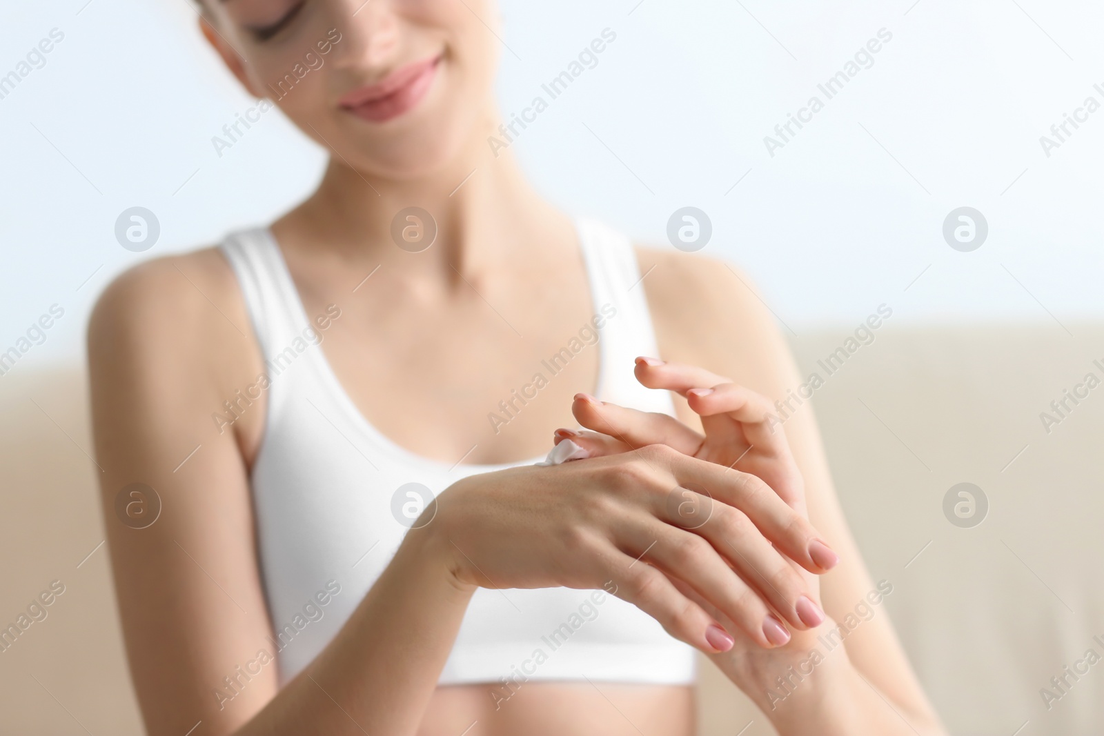 Photo of Young woman applying body cream at home