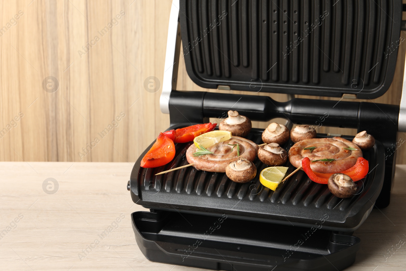 Photo of Electric grill with homemade sausages, mushrooms and bell pepper on wooden table, space for text