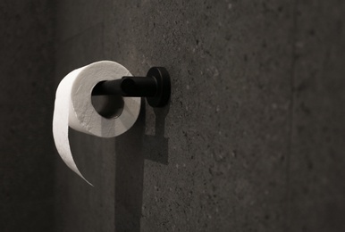 Toilet paper holder with roll mounted on dark wall. Space for text